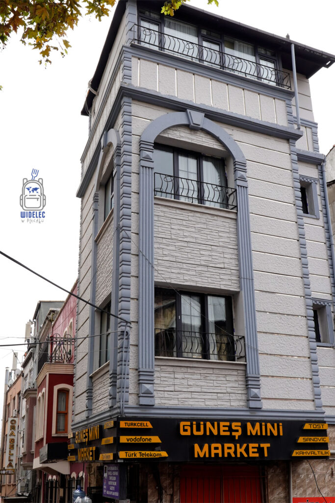 Zdjęcie przedstawiające charakterystyczny budynek w dzielnicy Fatih w Stambule. Na parterze znajduje się lokalny sklep Güneş Mini Market, oferujący przekąski, napoje oraz usługi telekomunikacyjne. Architektura budynku wyróżnia się szarymi zdobieniami i łukami nad oknami, które są typowe dla tej części miasta. Idealne miejsce do poznawania lokalnej kultury i życia mieszkańców. Stambuł - serce Turcji i kulturowa mieszanka Wschodu z Zachodem.