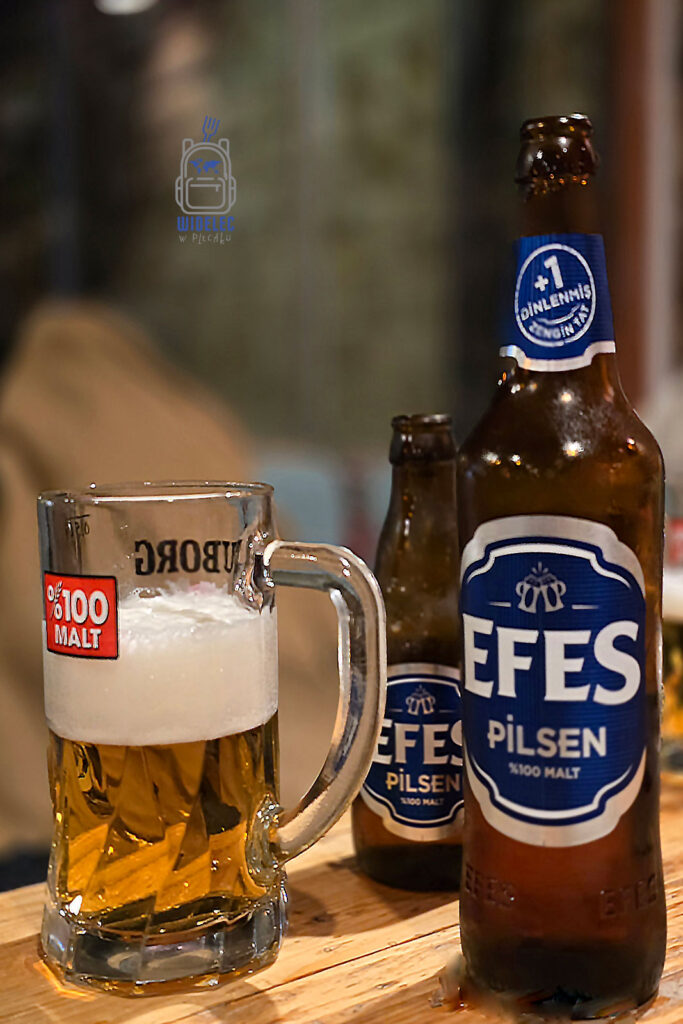 Butelka tureckiego piwa Efes Pilsen oraz kufel z piwem na drewnianym stole w klimatycznym lokalu, idealnym na relaks po zwiedzaniu Stambułu