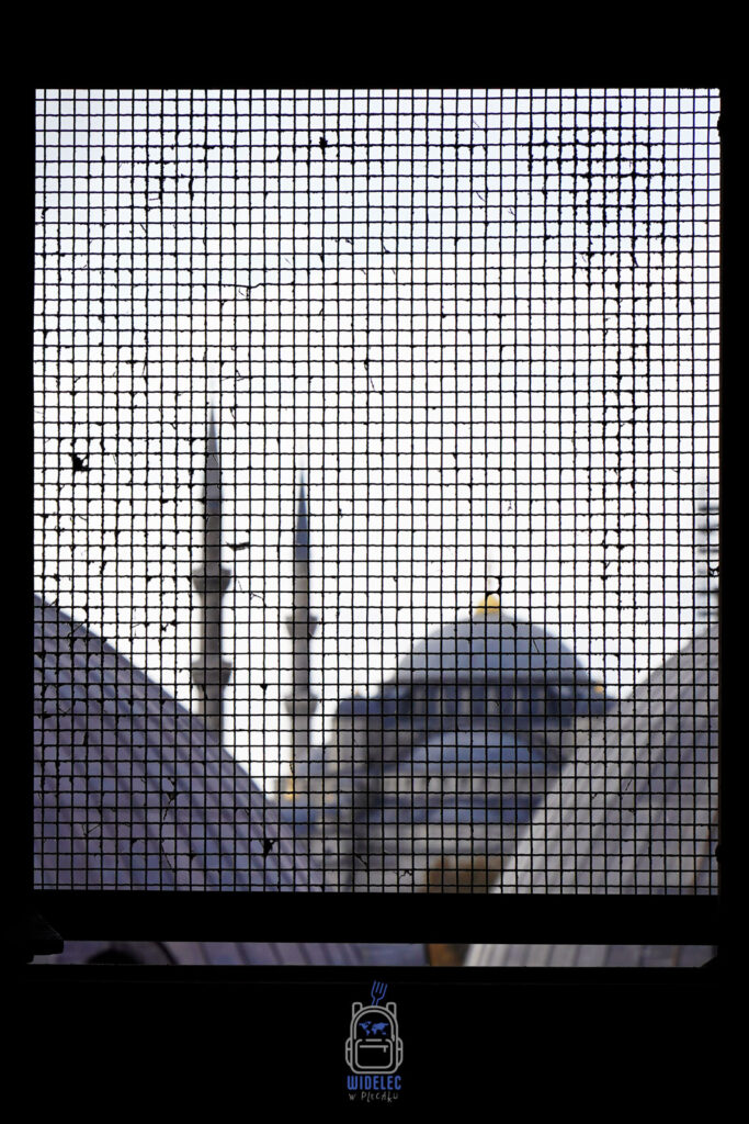 Rozmyty widok na meczet w Stambule widziany przez kratkę ochronną, symbolizujący kontrasty Turcji – od religii po współczesne wyzwania polityczne i społeczne.