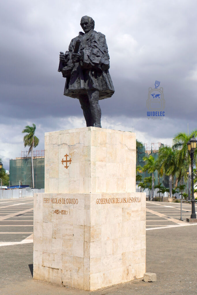 Zdjęcie przedstawia pomnik Fryderyka Nicolasa de Ovando, stojący na solidnym, marmurowym cokole w Santo Domingo. Pomnik wykonany jest z brązu i przedstawia Ovando w pełnej postaci, trzymającego w lewej ręce książkę, co może symbolizować jego rolę gubernatora i prawnika. Na cokole znajduje się inskrypcja z jego imieniem oraz datami życia (1461-1511) i tytułem "Gobernador de la Isla Española". Tło obrazu wypełniają palmy i modernistyczne budowle, co dodaje kontrastu historycznej postaci z nowoczesnym miastem
Dominikana – od wschodu do zachodu i z południa na północ