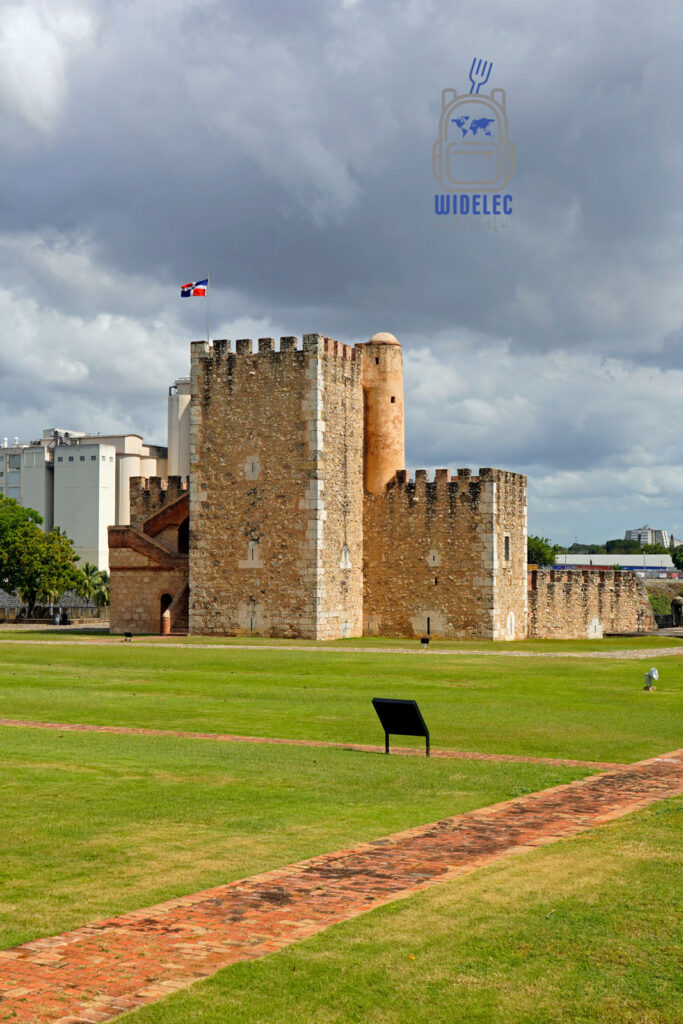 Zdjęcie przedstawiające Fort Ozama w Santo Domingo, jedną z najstarszych europejskich budowli wojskowych na Karaibach, widok na wysoką, kamienną strukturę z charakterystycznymi wieżami i murem obronnym, na tle dynamicznego nieba. Widać też flagę Dominikany powiewającą na wietrze, co podkreśla historyczne znaczenie miejsca. Idealne tło dla artykułu o dziedzictwie kulturowym i historycznych zabytkach Karaibów
Dominikana - z wschodu na zachód - z południa na północ