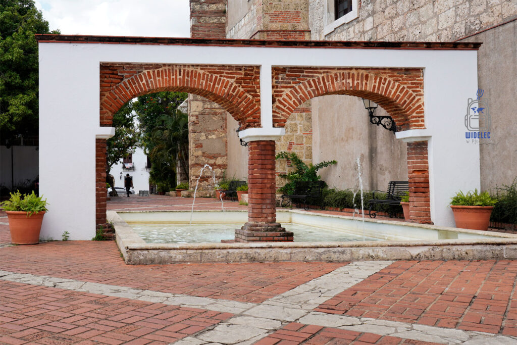 Zdjęcie ukazuje malowniczy dziedziniec z ceglanymi arkadami w Santo Domingo, który charakteryzuje się spokojną i urokliwą atmosferą. W centrum dziedzińca znajduje się prostokątny basen z fontanną, otoczony kwiatowymi doniczkami i ławkami, idealne miejsce na chwilę relaksu. Czerwone ceglane łuki dodają charakteru, tworząc piękny kontrast z białymi ścianami i kamiennymi elementami architektonicznymi. Scena ta doskonale oddaje ducha starych, kolonialnych miast
Dominikana – Z wschodu na zachod - z południa na północ
