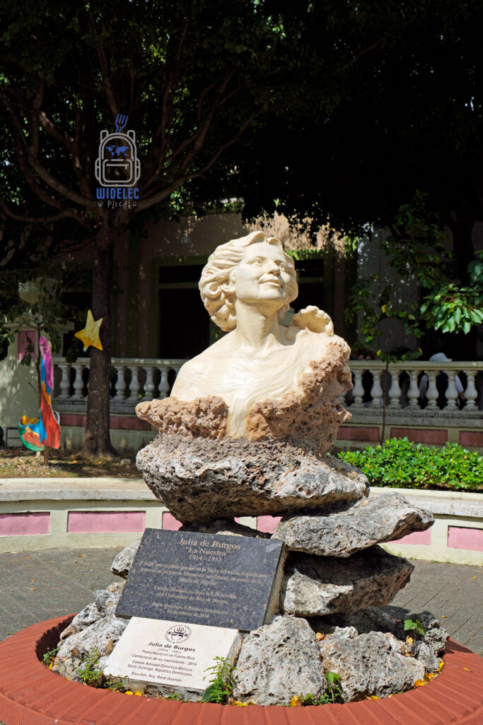 Zdjęcie przedstawia pięknie wykonaną rzeźbę portorykańskiej poetki, Julii de Burgos, znanej jako "La Nuestra". Rzeźba umieszczona jest na ozdobnym cokole z tabliczkami informacyjnymi, w otoczeniu zadbanego parku z licznymi drzewami i balustradą w tle. Statua, przedstawiająca Julię de Burgos z patrzącym w niebo wzrokiem, wykonana jest z jasnego materiału, co nadaje jej wyrazisty i inspirujący charakter. Pomnik ten jest umiejscowiony w parku w Santo Domingo i stanowi hołd dla tej wybitnej postaci literatury portorykańskiej
Dominikana – od wschodu do zachodu i z południa na północ