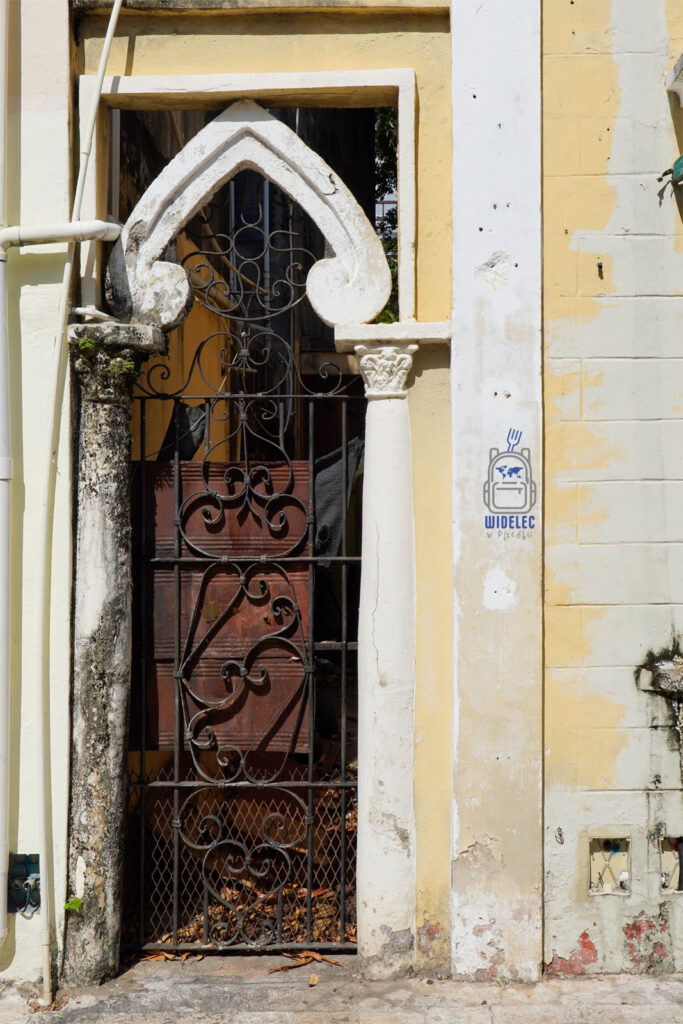 djęcie ukazuje starannie zdobioną bramę wejściową w Santo Domingo. Widoczna jest żółta, łukowata architektura z ozdobnymi, kutymi żelaznymi kratami, które dodają elegancji i charakteru. Fasada jest nieco zniszczona, co dodaje autentycznego uroku miejscu
Dominikana – Z wschodu na zachód - z południa na północ