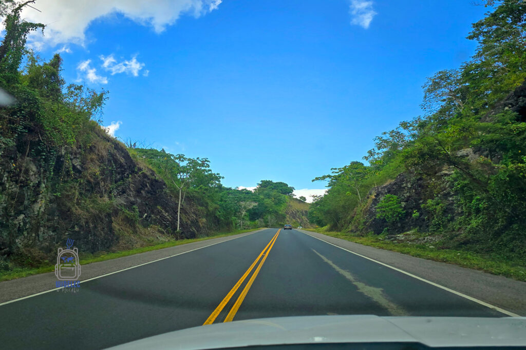 Malownicza droga otoczona zielonymi wzgórzami i tropikalną roślinnością, prowadząca przez górzysty teren. Niebieskie niebo z białymi chmurami dodaje uroku podróży samochodem. Idealna trasa na road trip i odkrywanie nieznanych zakątków natury. #podróże #roadtrip #widelecwplecaku
dominikana- z wschodu na zachód, z południa na północ