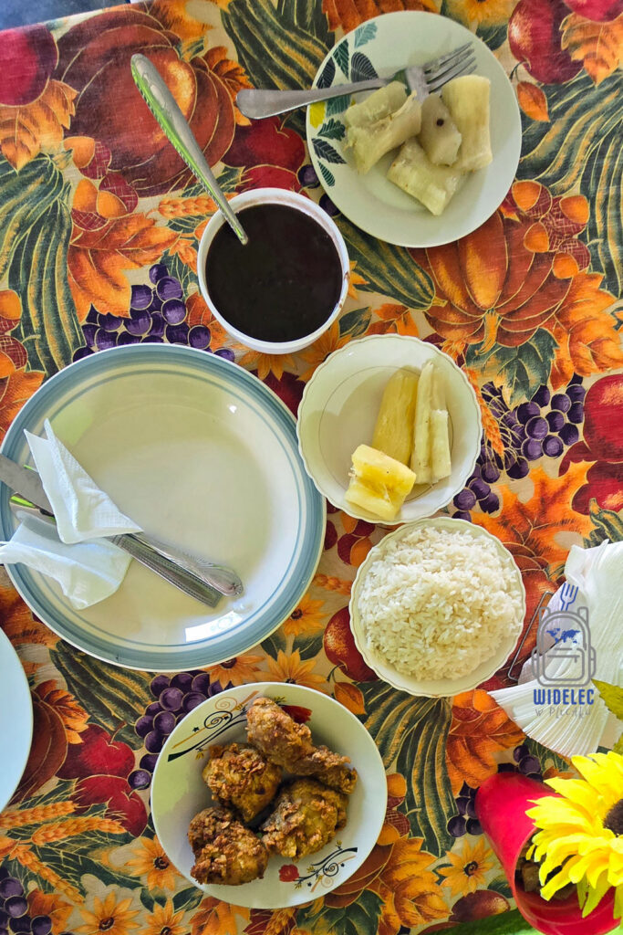 Zdjęcie przedstawia tradycyjne dominikańskie posiłki rozłożone na kolorowym obrusie z motywem owocowym. Na talerzach znajduje się różnorodność lokalnych dań, w tym smażony kurczak, biały ryż, ugotowane banany plantain oraz miseczka z czarną fasolą. Całość komponuje się w pełny, kolorowy obraz dominikańskiego stołu
#widelecwpleacaku
#dominikana - z wschodu na zachód - z południa na północ