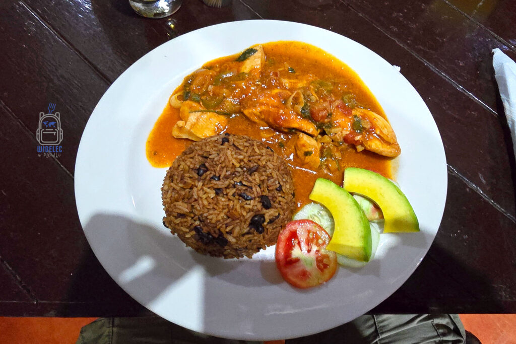 Tradycyjny dominikański obiad, Pollo a la Criolla, serwowany na białym talerzu. Danie składa się z aromatycznego, przyprawionego ryżu z fasolą, pikantnego kurczaka w kreolskim sosie oraz świeżych dodatków w postaci plasterków awokado i pomidora.
#widelecwpleacaku
#dominikana - z wschodu na zachód - z południa na północ