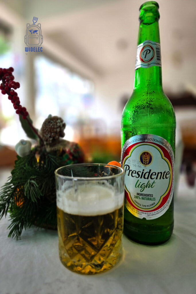 Butelka piwa Presidente Light, otoczona świątecznymi dekoracjami, stoi na jasnym stole w Dominikanie. To lekkie piwo typu pilsner jest znane ze swojego orzeźwiającego smaku i lekkości, idealne do spożywania w ciepłym, tropikalnym klimacie. Zdjęcie podkreśla autentyczny duch świąt w dominikańskim stylu
#widelecwpleacaku
#dominikana - z wschodu na zachód - z południa na północ