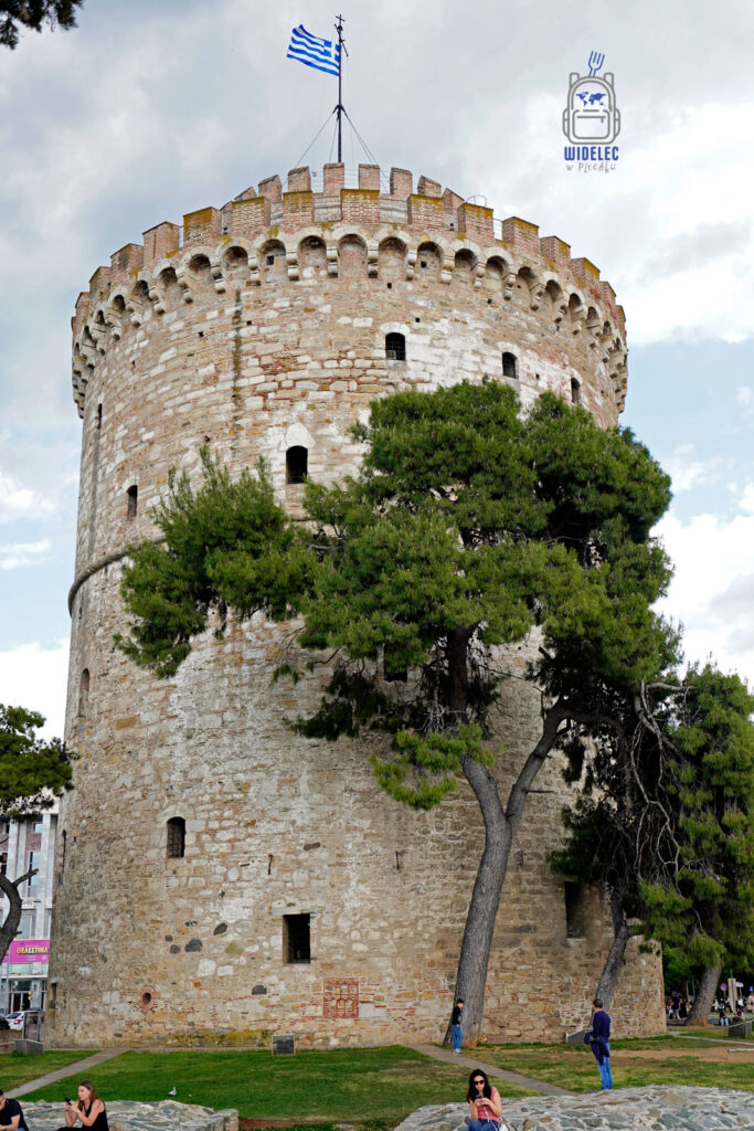 Biała Wieża w Salonikach otoczona drzewami, ludzie odpoczywający w cieniu