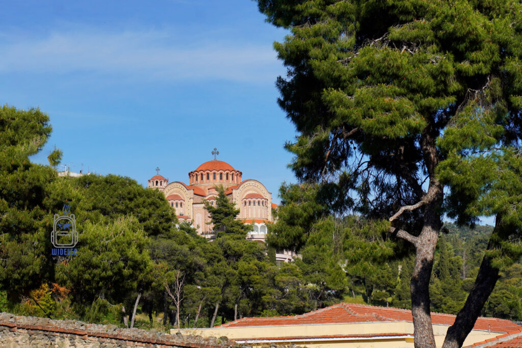 Cerkiew św. Grzegorza Palamasa w Salonikach, otoczona piniami i ukazana na tle błękitnego nieba, widok zza murów miasta