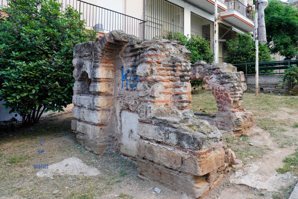 Fragment starożytnej lub bizantyjskiej ruiny z cegły i kamienia na tle współczesnego osiedla mieszkaniowego w Salonikach – symbol współistnienia epok w miejskiej przestrzeni.