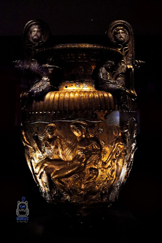 Złocony ceremonialny krater z mitologicznymi reliefami – starożytne greckie naczynie z bogato zdobioną powierzchnią przedstawiającą sceny z mitologii, ukazujące nagie postaci w dynamicznych pozach. Po bokach uchwyty ozdobione ludzkimi twarzami. Eksponat z muzeum archeologicznego w Salonikach.