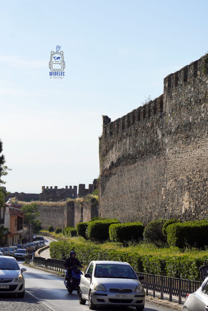 Potężne mury obronne Salonik biegnące wzdłuż ruchliwej ulicy – świadectwo wielowiekowej historii miasta w kontraście do współczesnego zgiełku.