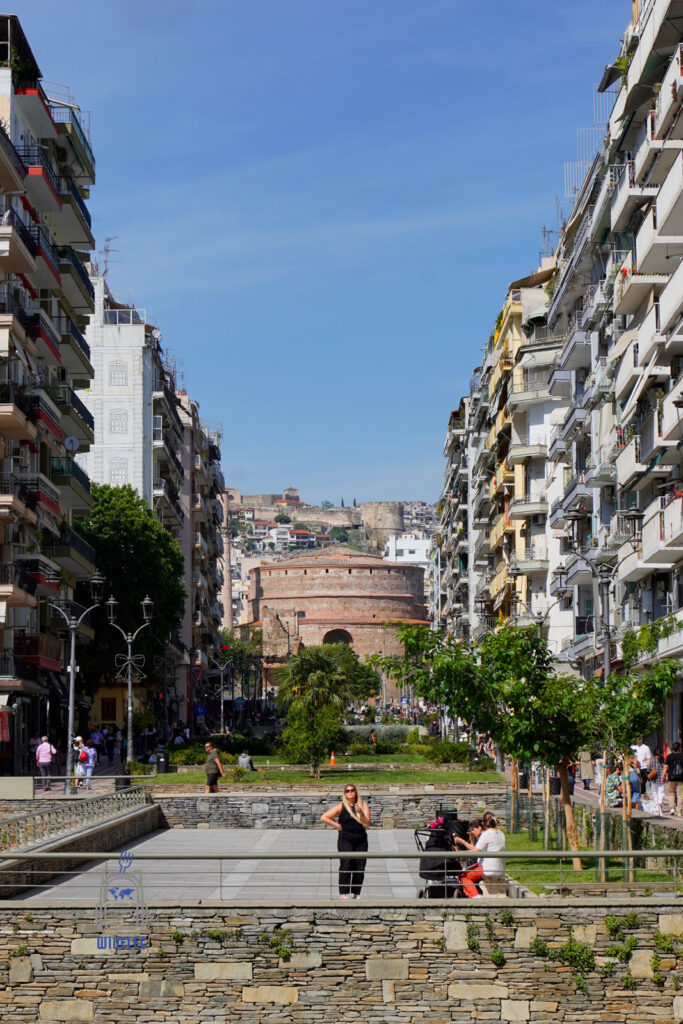 Widok na Rotundę Galeriusza w Salonikach, wpisaną w oś współczesnego miasta, z tłumem ludzi i zielenią na pierwszym planie