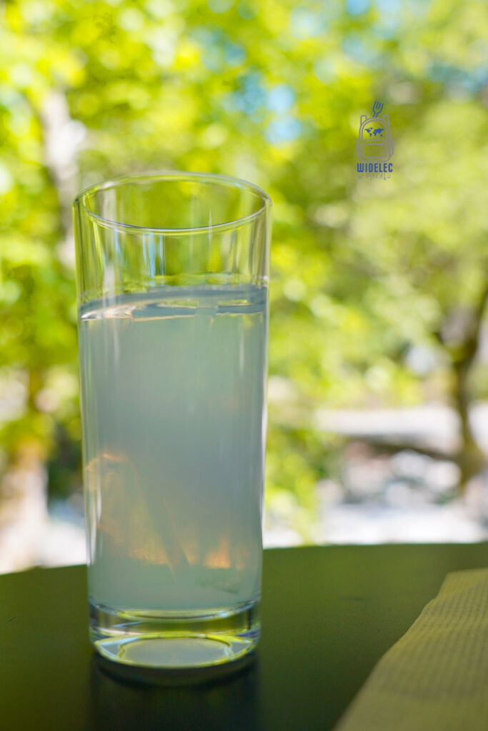 Szklanka ouzo z lodem podana na świeżym powietrzu, w cieniu platanów – orzeźwiający anyżowy napój symbolizujący grecki relaks i wakacyjny luz.