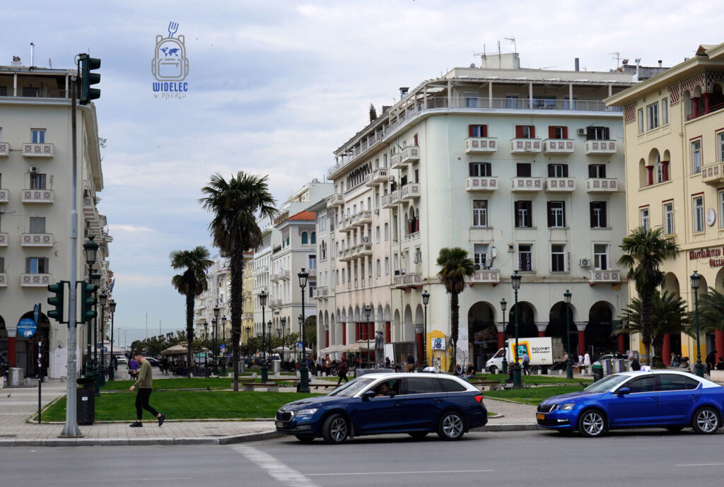 Plac Arystotelesa w Salonikach – elegancka zabudowa z arkadami, palmami i kawiarniami, tętniące życiem centrum miasta z widokiem na nadmorską promenadę.