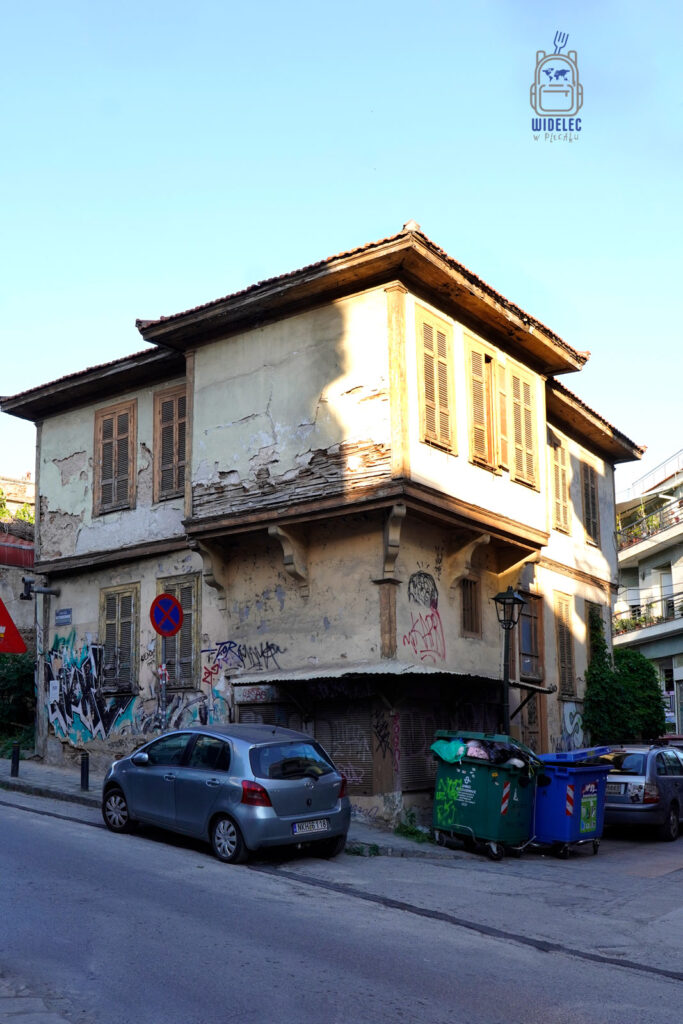 Stary, zniszczony dom z drewnianymi okiennicami i graffiti na ścianach w jednej z bocznych ulic Salonik – świadectwo miejskiego retro-chaosu i upływu czasu.