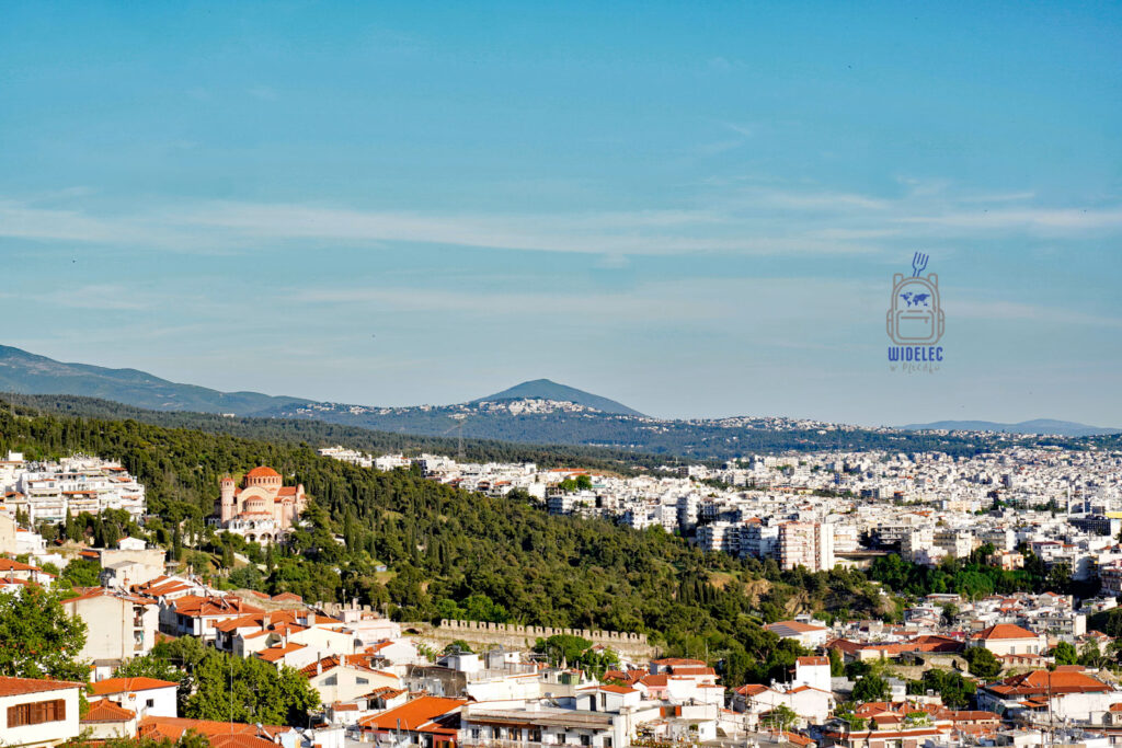 Panorama Salonik z czerwonymi dachami, otaczającymi zielonymi wzgórzami i widokiem na monumentalną cerkiew św. Pawła – ujęcie rozciągające się aż po horyzont.
