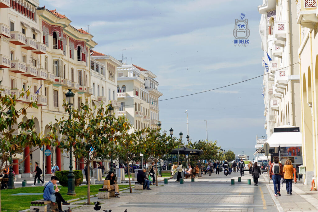 Spacer po reprezentacyjnej alei placu Arystotelesa w Salonikach, z widokiem na morze, elegancką architekturą i odpoczywającymi mieszkańcami w cieniu drzew.