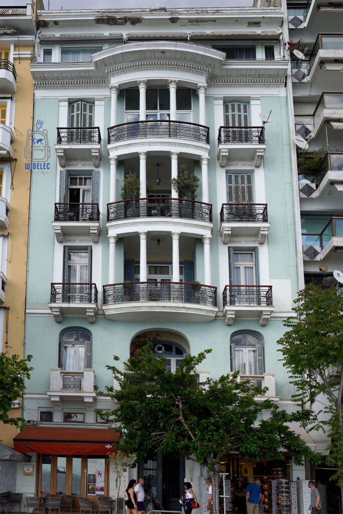 Elegancka neoklasycystyczna kamienica z kolumnowym balkonem przy nadmorskiej promenadzie w Salonikach – przykład architektury z przełomu XIX i XX wieku.