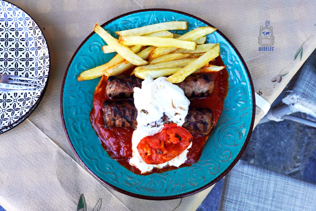 Sish kebab w greckim stylu – grillowane kotleciki z mięsa mielonego w sosie pomidorowym, podane z frytkami i jogurtem, serwowane w tawernie.