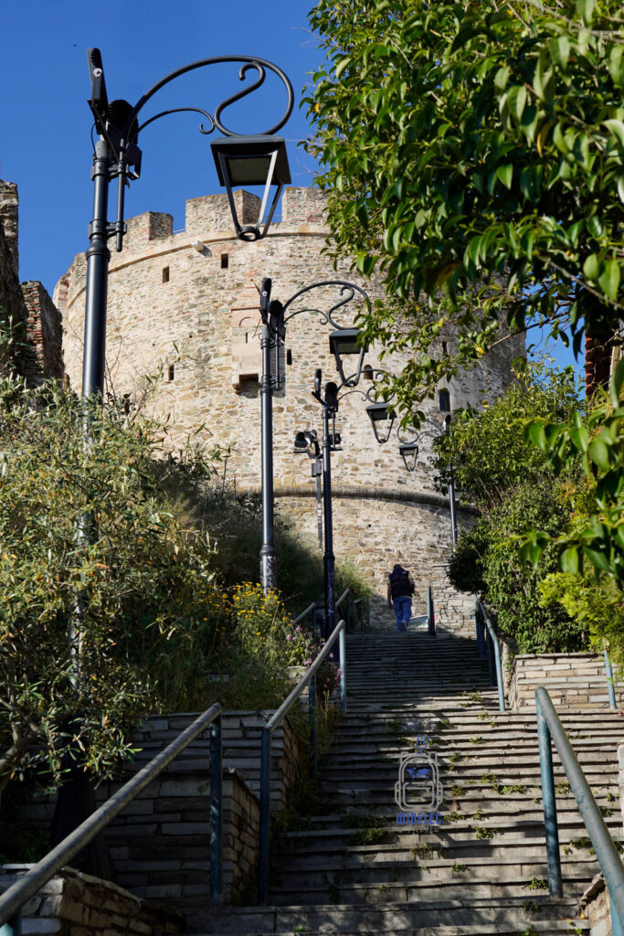 Kamienne schody prowadzące do wieży Trigoniou w Salonikach, otoczone latarniami i zielenią – malownicze wejście do jednego z najlepiej zachowanych punktów dawnych fortyfikacji.