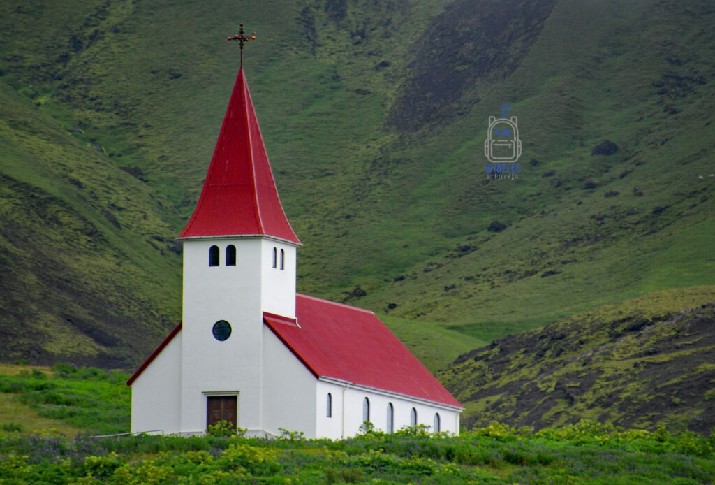 Islandia – biały kościół z czerwonym dachem w miasteczku Vík í Mýrdal, otoczony zielonymi wzgórzami i surową przyrodą południowego wybrzeża – widelecwplecaku.pl