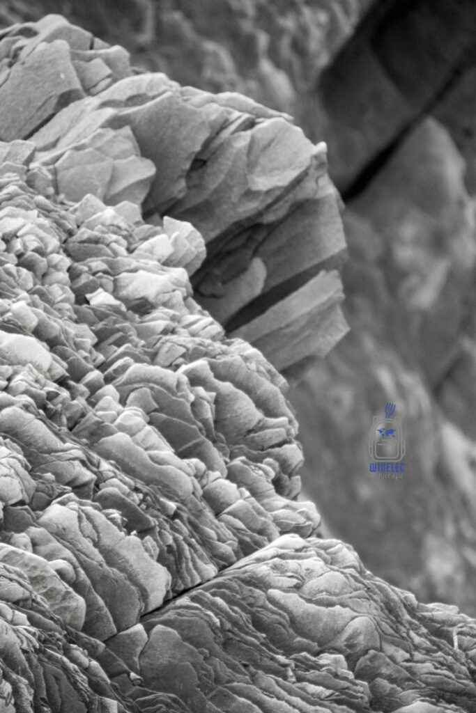 Islandia – czarno-białe zbliżenie na skalne formacje o fantazyjnych kształtach, przypominających warstwy i pęknięcia lawy; surowa natura – widelecwplecaku.p