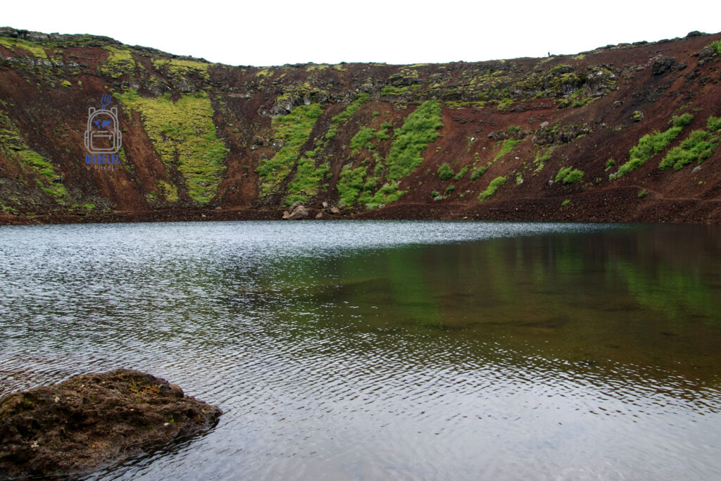 Jezioro w kraterze Kerið (Kerid) w południowej Islandii – spokojna tafla wody odbijająca czerwone i zielone zbocza wulkanicznego krateru, kontrast natury i surowego krajobrazu, widelecwplecaku.pl