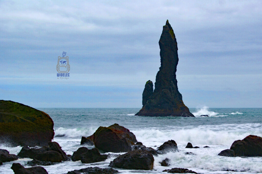 Reynisdrangar – monumentalna bazaltowa formacja skalna wystająca z oceanu przy czarnej plaży w Vik, południowa Islandia, fale rozbijające się o kamieniste wybrzeże, widelecwplecaku.pl