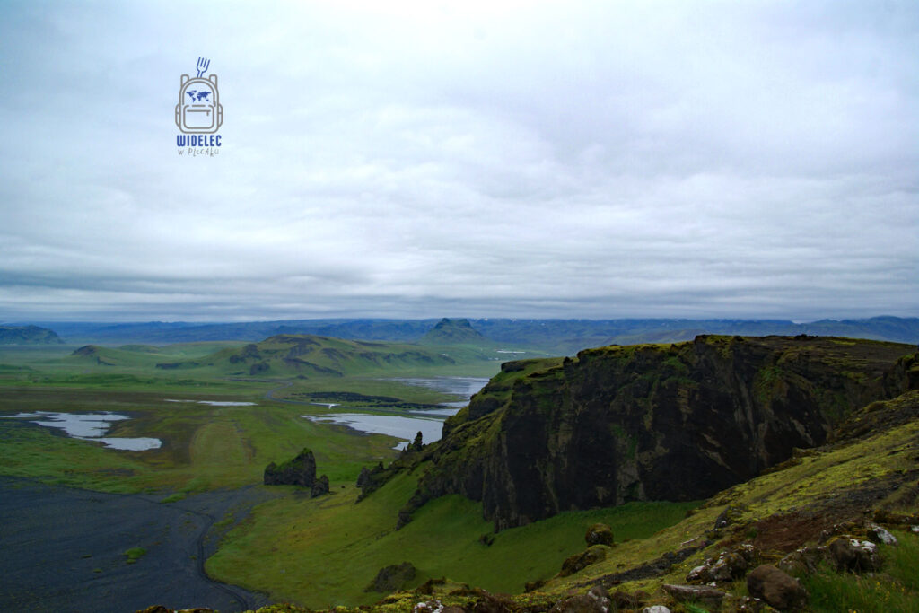 widok na zielone doliny, strome klify i czarne pola lawy pod pochmurnym niebem; surowy krajobraz południa wyspy – widelecwplecaku.pl