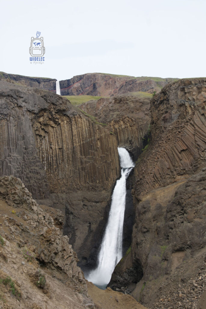 Wodospad Litlanesfoss otoczony strzelistymi bazaltowymi kolumnami, a w tle widoczny Hengifoss – atrakcja wschodniej Islandii, widelecwplecaku.pl