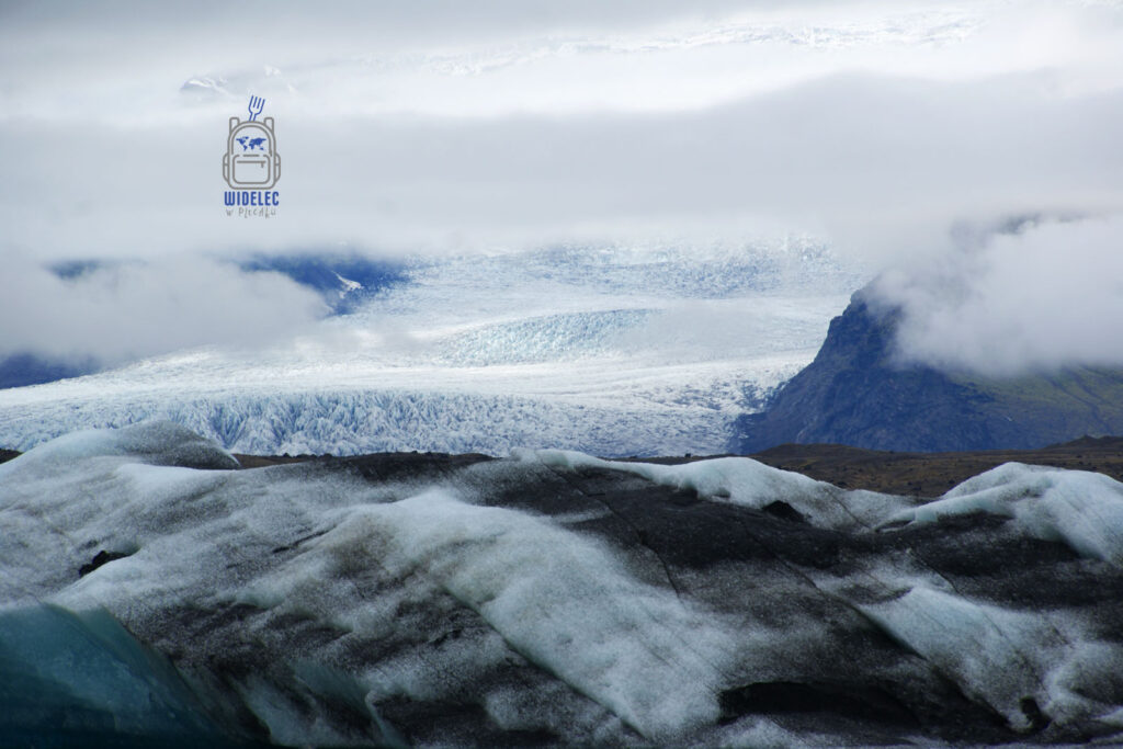 odowiec spowity chmurami, widoczna lodowa pokrywa i ciemne skały w surowym krajobrazie południa wyspy; majestatyczna natura – widelecwplecaku.pl