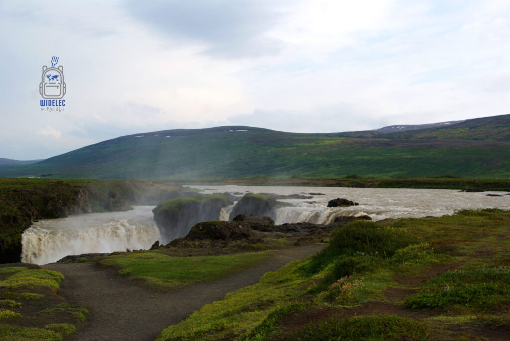 Wodospad Goðafoss spadający szeroką kaskadą w otoczeniu zielonych wzgórz, widelecwplecaku.pl