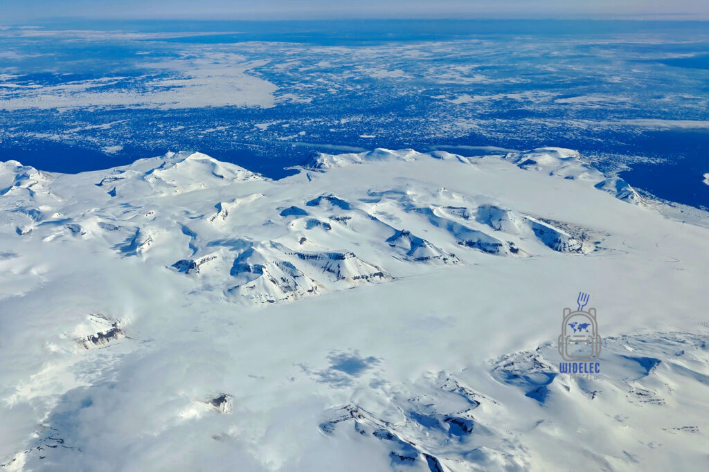 Widok na ośnieżone góry, lodowce i fiordy Svalbardu z okna samolotu podczas lotu do Longyearbyen.