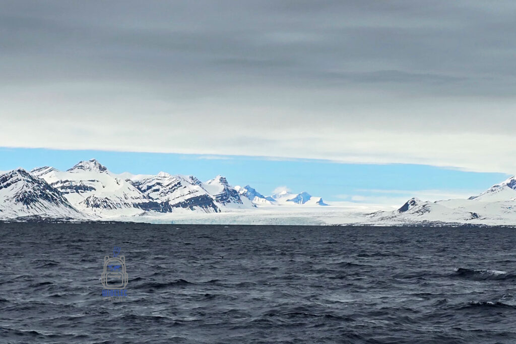 ciemnoniebieskie morze, w tle lodowiec spływający do morza, zachmurzone niebo. Svalbard.