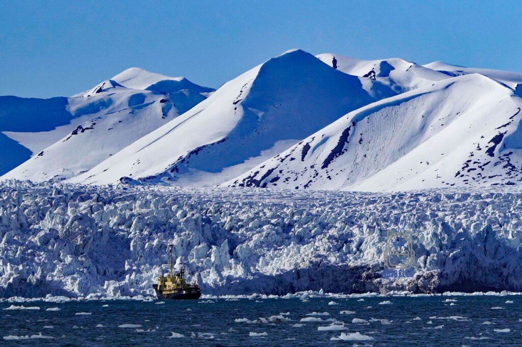ośnieżone szczyty nad lodowcem, na morzu mały statek badawczy. Svalbard. Arktyka