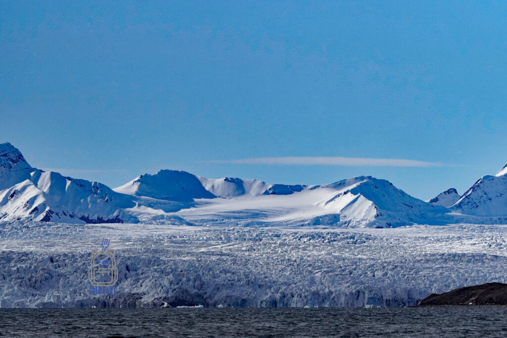 lodowiec oraz mocno ośnieżone wzgórza pod błękitnym niebem. Svalbard, Arktyka