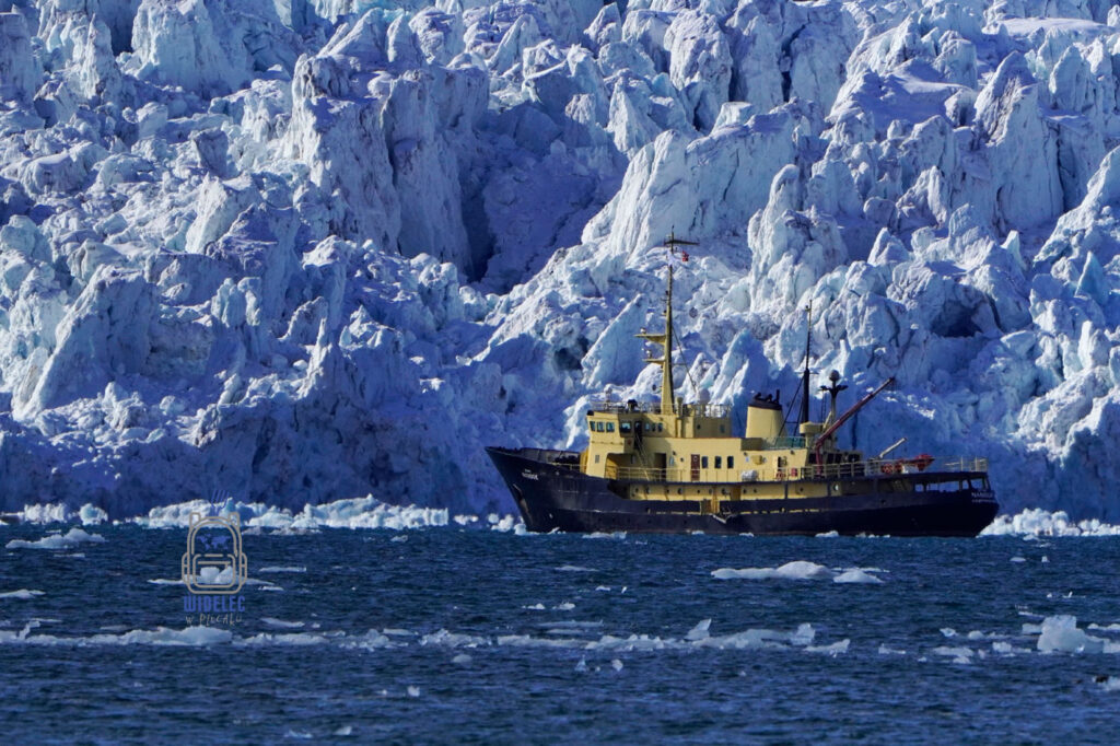 żółtoczarny statek badawczy na tle potężnego lodowca. Svalbard, Arktyka