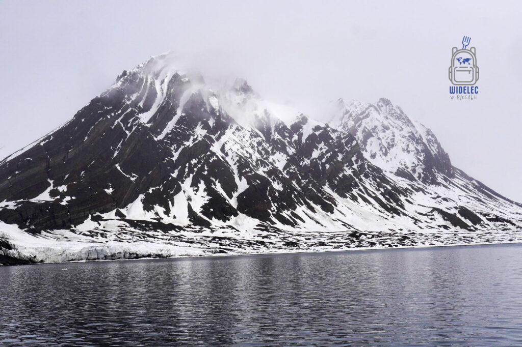 Pojedynczy szczyt lekko oprószony śniegiem znikający w chmurze na Svalbard, Arktyka