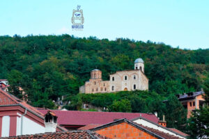 Zabytkowa prawosławna cerkiew Chrystusa Zbawiciela (Sveti Spas) w Prizren w Kosowie, położona na zielonym zboczu wzgórza ponad dachami starego miasta. Kamienna świątynia z charakterystycznymi ceglanymi zdobieniami, niewielką kopułą i przylegającą do niej większą, częściowo odbudowaną konstrukcją wyróżnia się na tle gęsto zalesionego wzgórza. Do cerkwi prowadzi kamienna ścieżka, po której spacerują turyści. Na pierwszym planie widoczne są czerwone dachówki zabudowań historycznego centrum Prizren