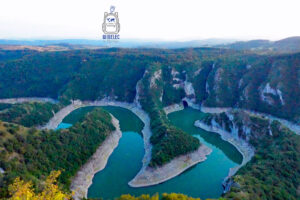 Panoramiczny widok z punktu widokowego Molitva (1247 m n.p.m.) na malownicze meandry rzeki Uvac w południowo-zachodniej Serbii. Turkusowo-zielona woda tworzy głębokie zakola wokół porośniętych lasem półwyspów, otoczonych stromymi wapiennymi zboczami. W oddali rozciągają się zalesione wzgórza rezerwatu przyrody Uvac.