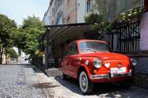 Czerwona Zastava 750, kultowy samochód dawnej Jugosławii, zaparkowana na brukowanej uliczce Skadarlija w Belgradzie w Serbii. Zabytkowe auto ozdobione białymi sercami stoi przed restauracją Boembar, w otoczeniu starych kamienic, kwiatów i zielonych drzew