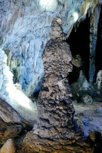 Potężny stalagmit o nieregularnej, kalafiorowatej powierzchni we wnętrzu Jaskini Lodowej (Ledena Pećina) w rezerwacie przyrody Uvac w Serbii. Wysoka formacja wapienna wyrasta z dna jaskini, a w tle widoczne są liczne stalaktyty, nacieki przypominające kamienne zasłony oraz ciemne skalne zakamarki. Białe i niebieskawe oświetlenie podkreśla niezwykłe kształty i fakturę podziemnych formacji.